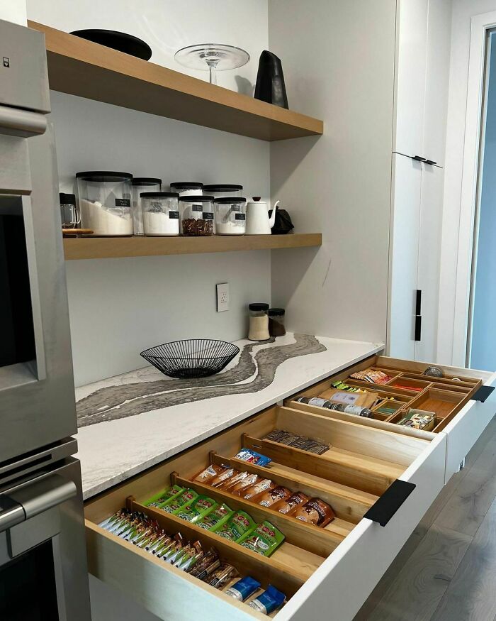Organized kitchen with labeled jars on shelves and neatly arranged snacks in drawer.