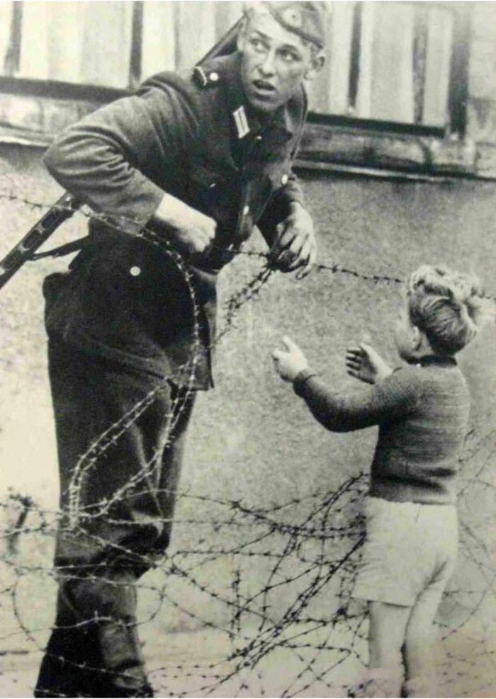 1961. East German Soldier Ignores Orders To Let No One Pass By Helping A Young Boy Cross The Newly Built Berlin Wall, To Reunite With His Family
