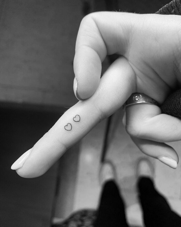 Close-up of a hand with two small heart tattoos on the finger, representing celebrity tattoos.