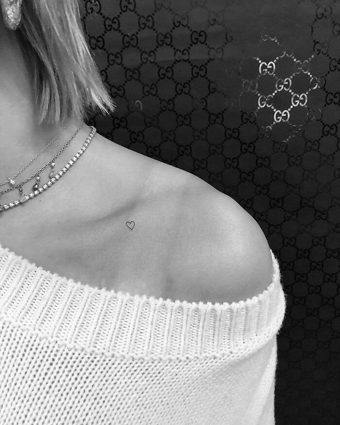 Minimalist celebrity tattoo of a small heart on the shoulder, wearing a white sweater.