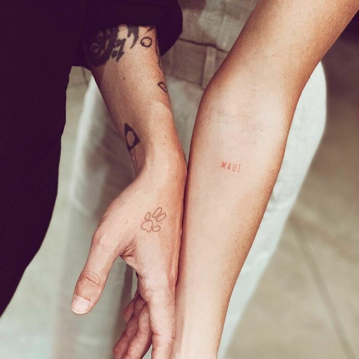 Close-up of hands with celebrity tattoos, one with a paw print and another with "MAUI" text.