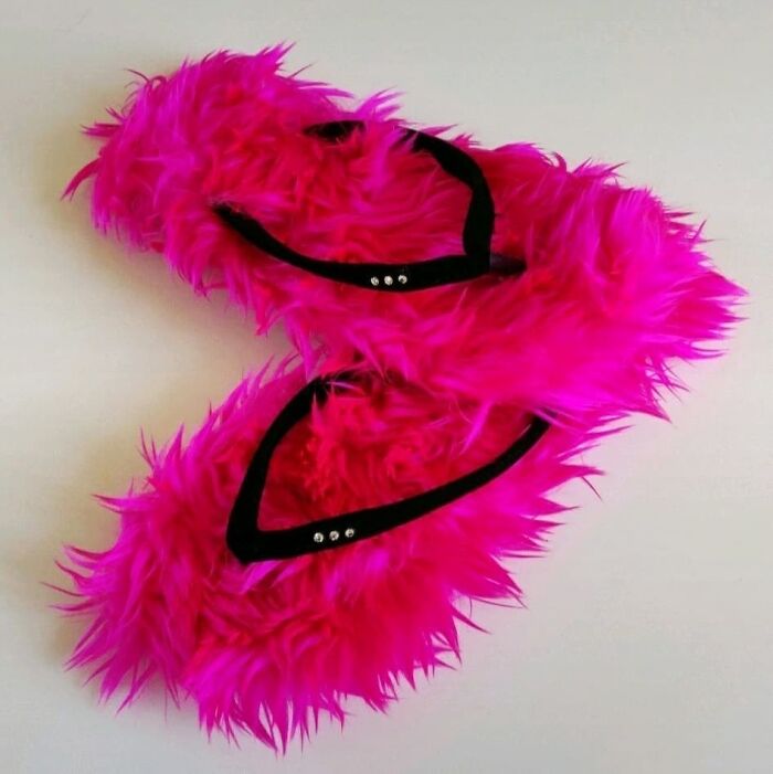 Bright pink fuzzy weird shoes with black straps on a white background.