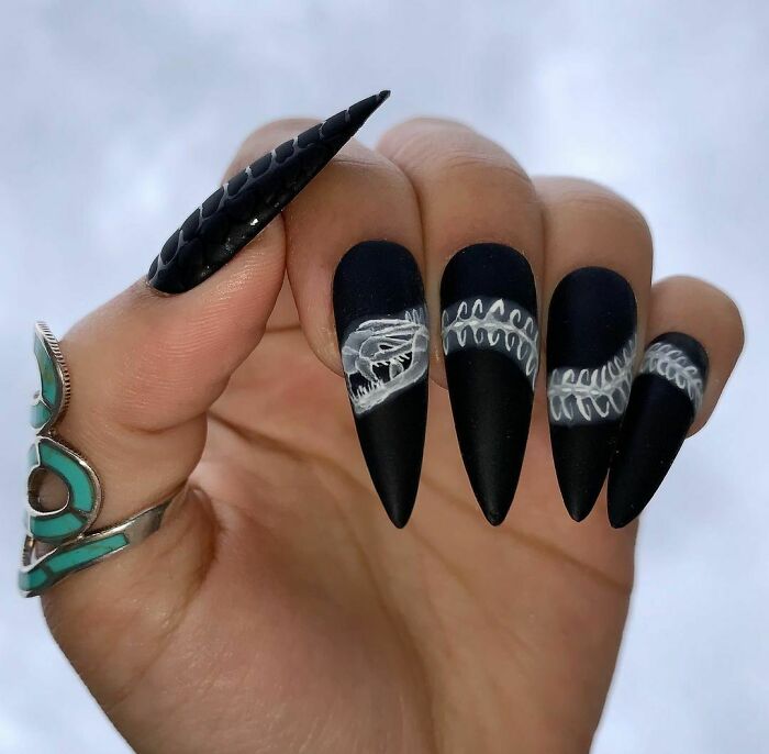 Black matte stiletto nails featuring detailed white skeleton and bone art, showcasing creative nail art ideas.