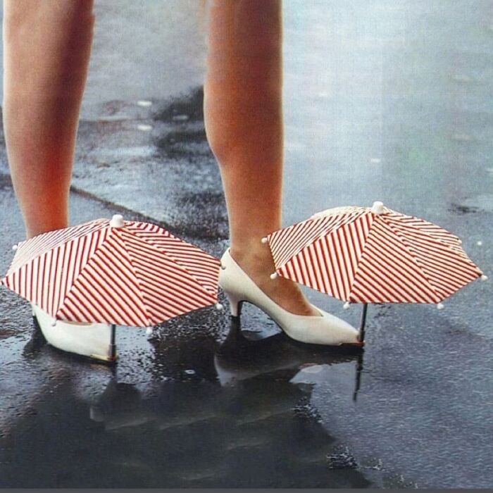 Weird shoes with red and white striped umbrellas attached, worn on a wet surface.