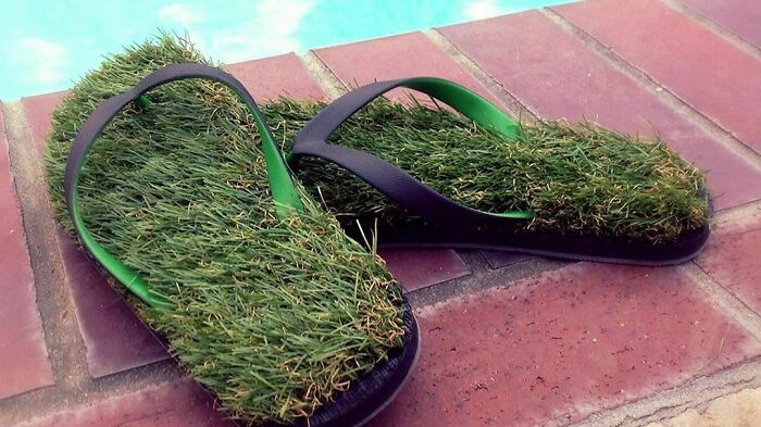 Weird shoes designed to look like grass flip-flops placed by a poolside.