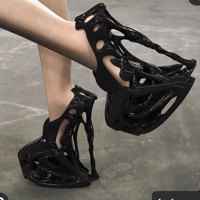 Black weird shoes with intricate, abstract design on a gray surface.