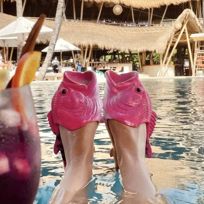 Pink fish-shaped shoes worn by a pool, showcasing weird footwear fashion.