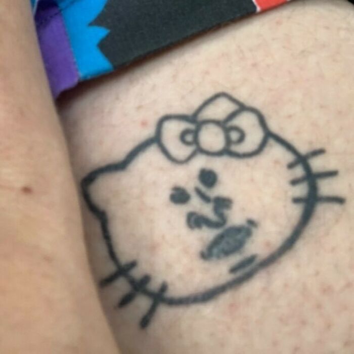 Poorly drawn cat tattoo with bow on skin, showcasing a design that wasn't thought through.