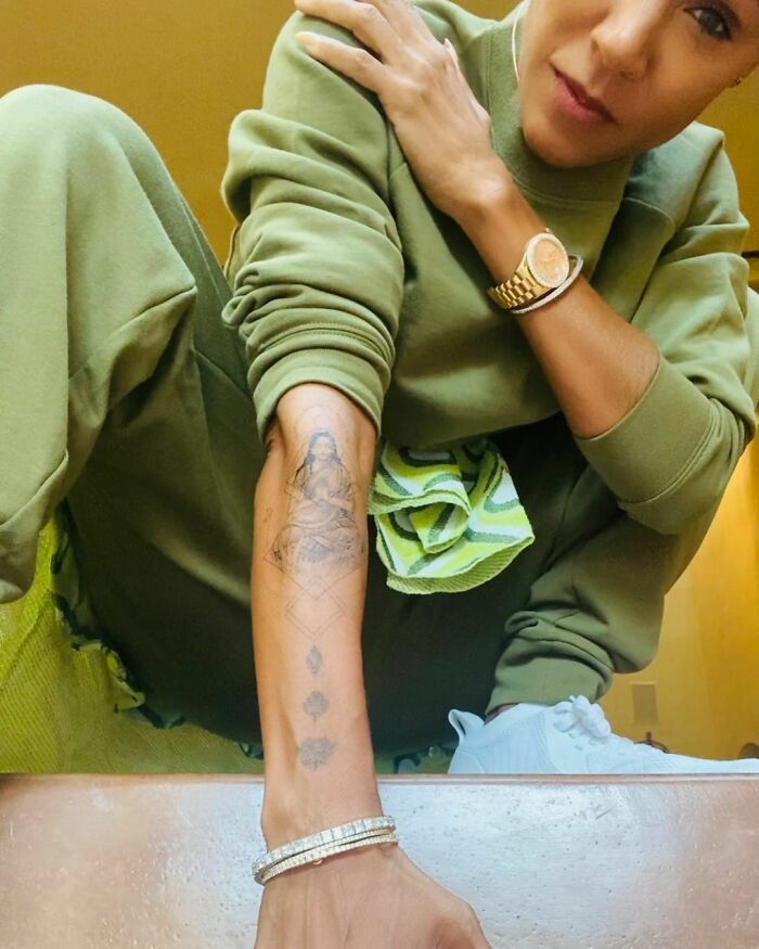 Celebrity showing arm tattoos while wearing a green outfit, featuring wrist bracelets and a watch.