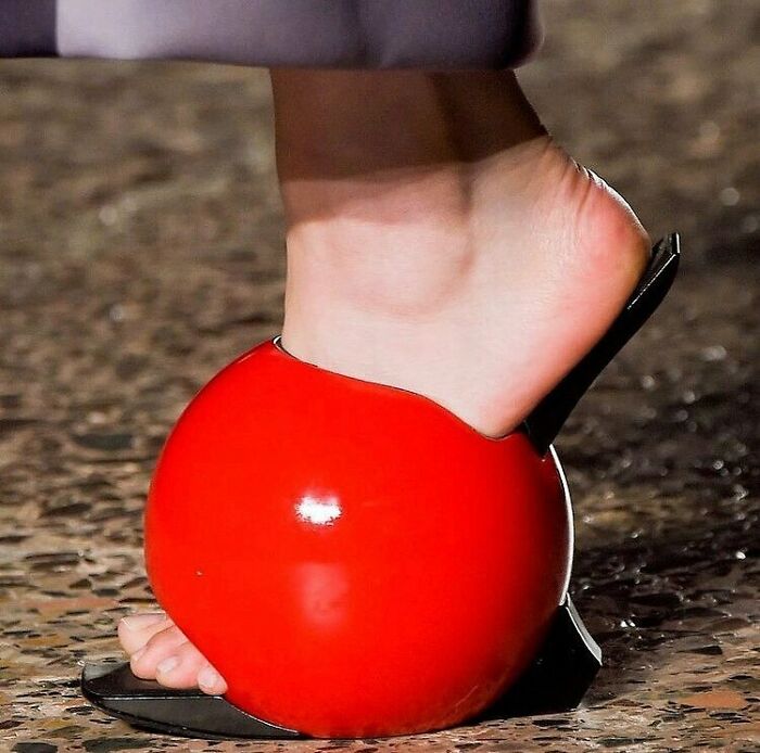 Weird shoes resembling red balls with an open-toe design worn on a stone pavement.