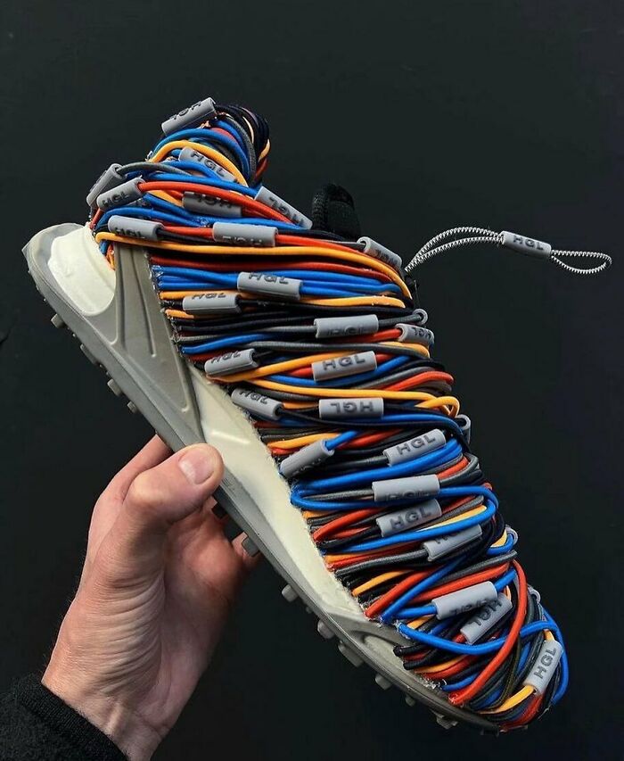Hand holding a weird shoe wrapped with colorful cables, showcasing unusual footwear design.