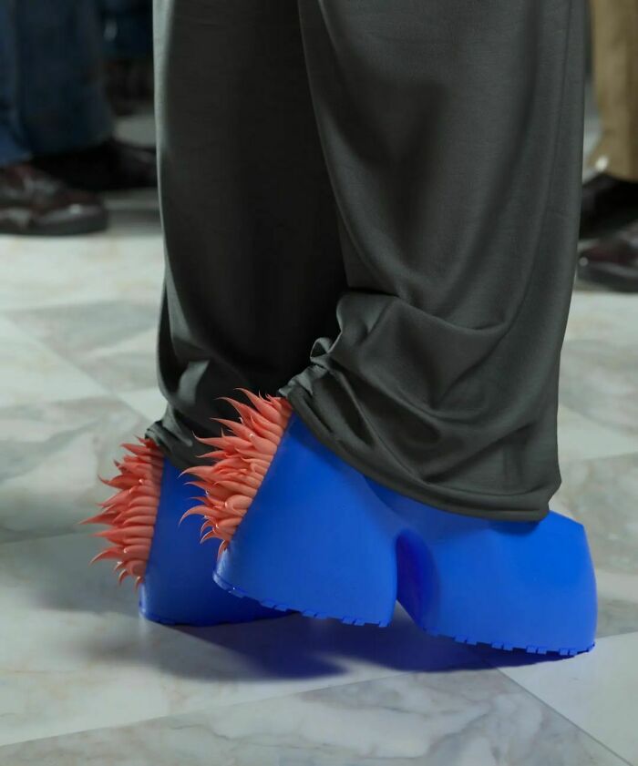 Weird shoes with blue platforms and red spikes, worn under gray pants on a marble floor.