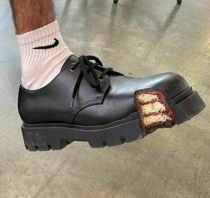 Weird shoe with black leather design featuring a slice of cake at the toe, worn with white socks.