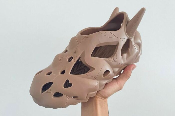 A hand holding a tan sculpted shoe resembling a futuristic creature, showcasing weird shoe design.