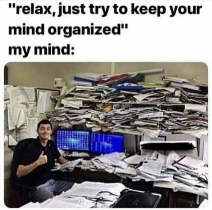 A cluttered desk covered in papers with a smiling person giving a thumbs up, illustrating a disorganized mind meme.