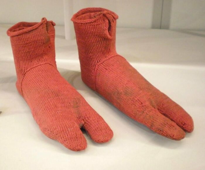Unusual red knitted shoes with split toes displayed on a white surface.