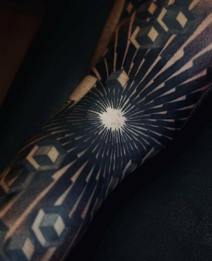 Geometric tattoos with intricate patterns and a central radiating design on an arm.
