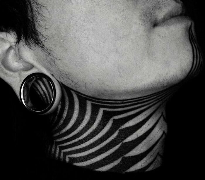 Close-up of a geometric tattoo on a person's neck with ear gauge, showcasing intricate pattern work.