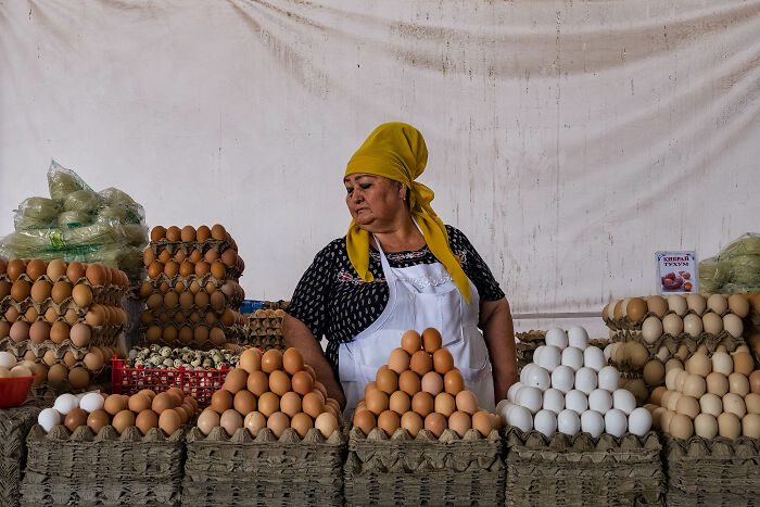 Woman vendor wearing yellow headscarf and apron organizing eggs at market, representing women and breaking stereotypes.