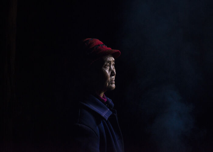 Elderly woman wearing a red hat in low light, symbolizing strength and breaking stereotypes for women in photography.