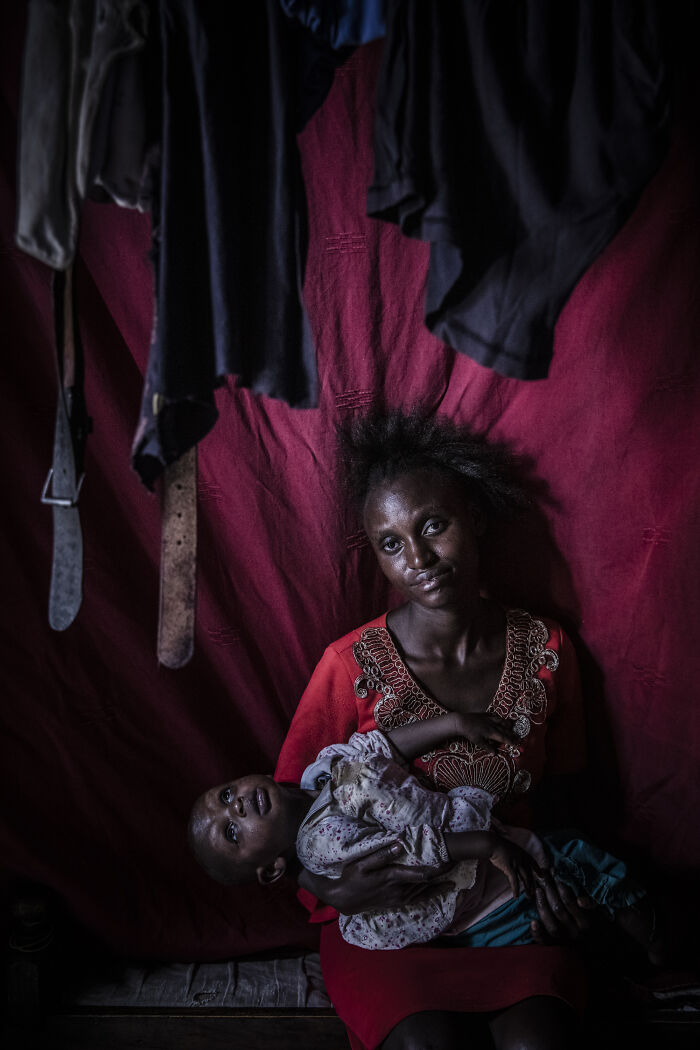 Woman holding child inside dimly lit room, highlighting strength and breaking stereotypes in a powerful portrait.