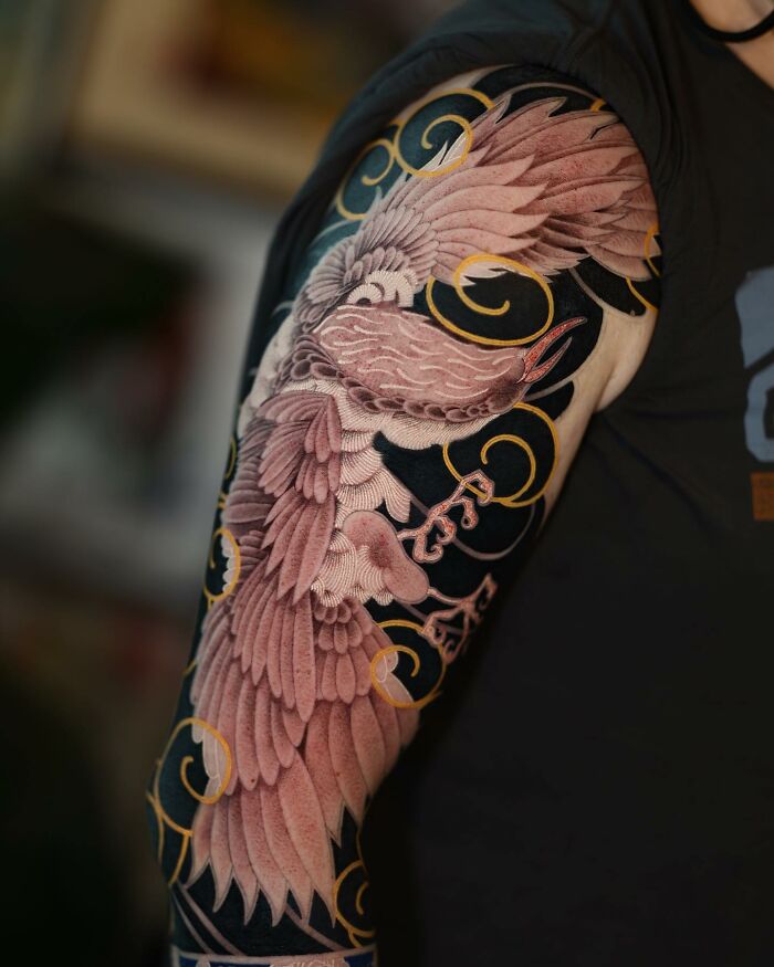 Mesmerizing tattoo by Korean artist featuring an intricate crane design on an arm with gold and black detailing.