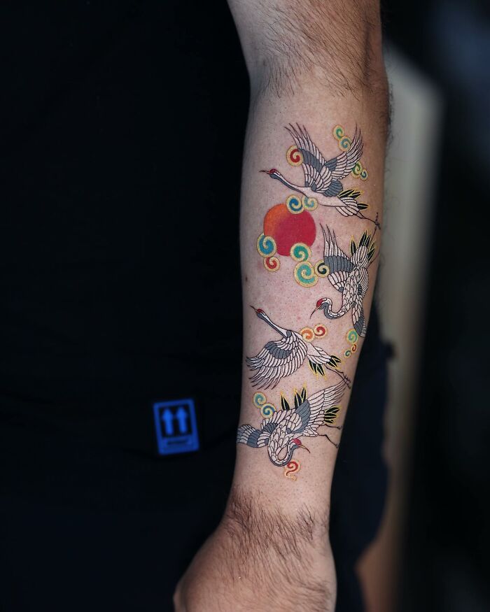 Korean artist's mesmerizing tattoo featuring cranes and a red sun on a person's arm.