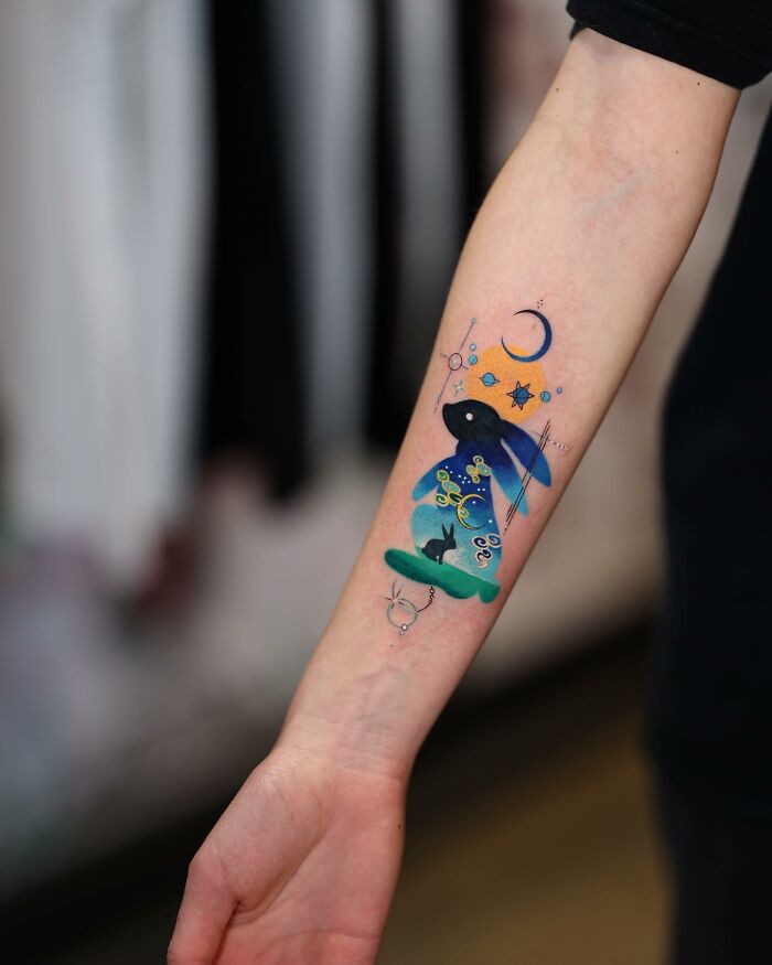 Mesmerizing tattoo by Korean artist featuring a colorful, abstract rabbit and celestial elements on an inner forearm.