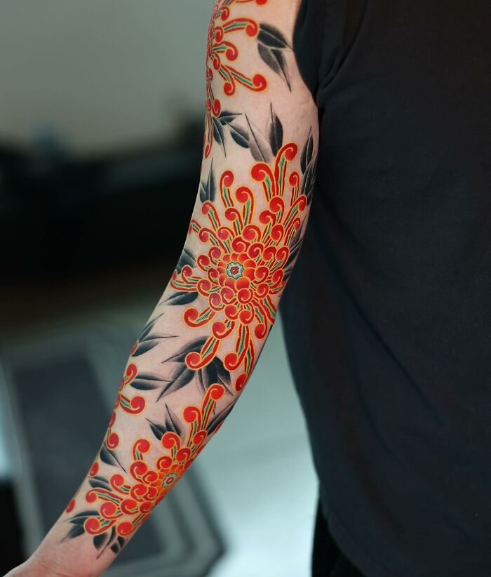 Mesmerizing tattoo by Korean artist featuring a vibrant red floral design with black leaf accents on arm.
