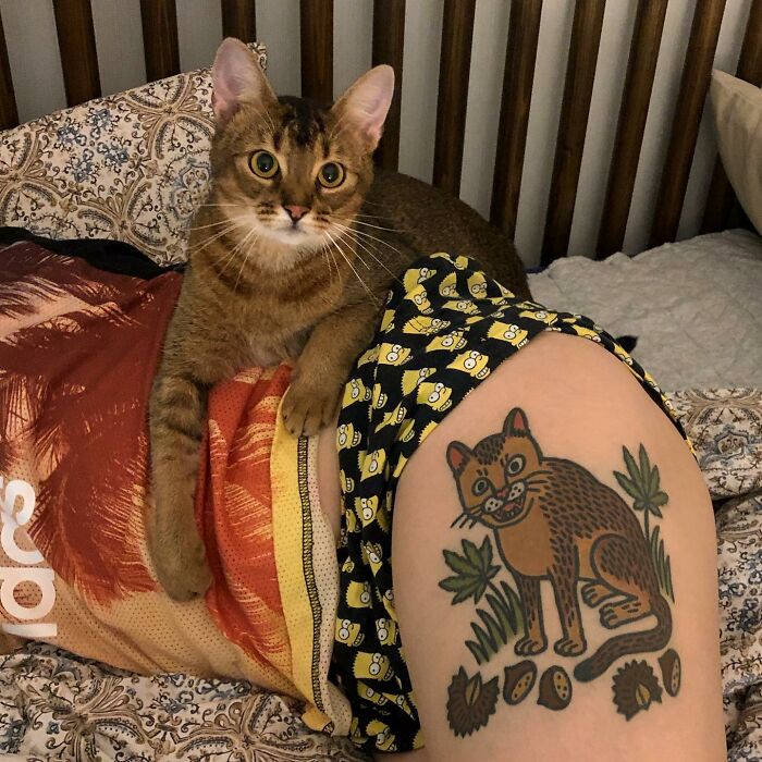 Cat beside a tattoo of a stylized feline, showcasing a unique approach to representing animals in tattoo art.
