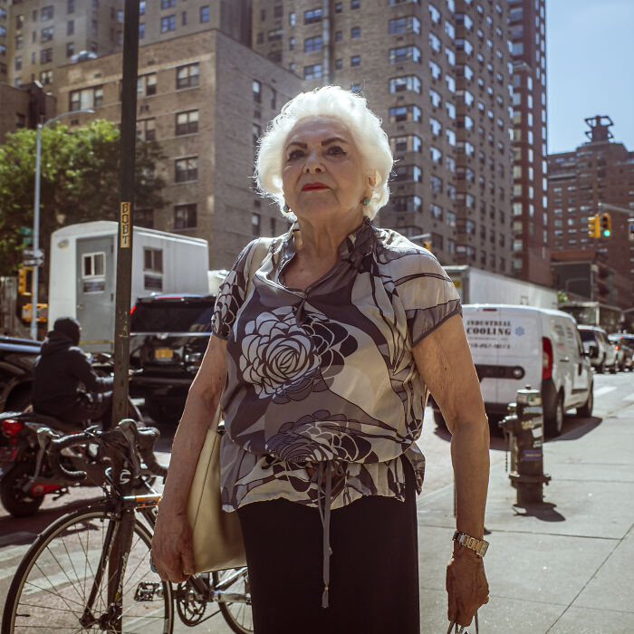 Elderly woman standing confidently in urban street, representing women and breaking stereotypes in a modern city setting.