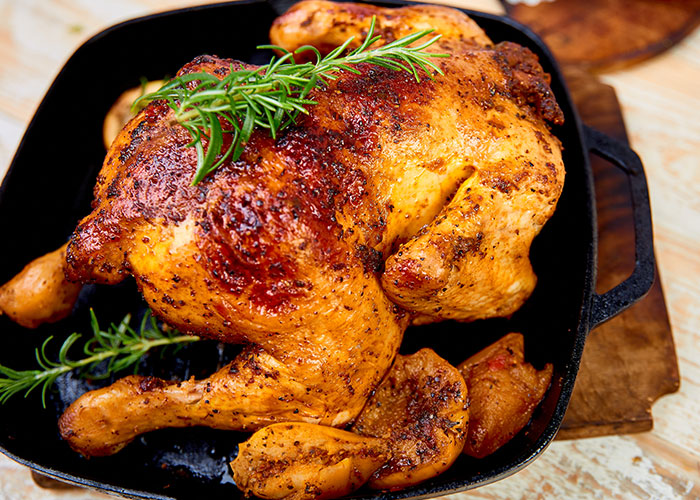 Roasted chicken with herbs in a pan, illustrating American cuisine and seemingly healthy foods debated internationally.