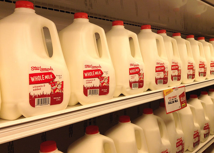 Rows of whole milk gallon jugs on store shelves symbolizing seemingly healthy American cuisine choices banned elsewhere.