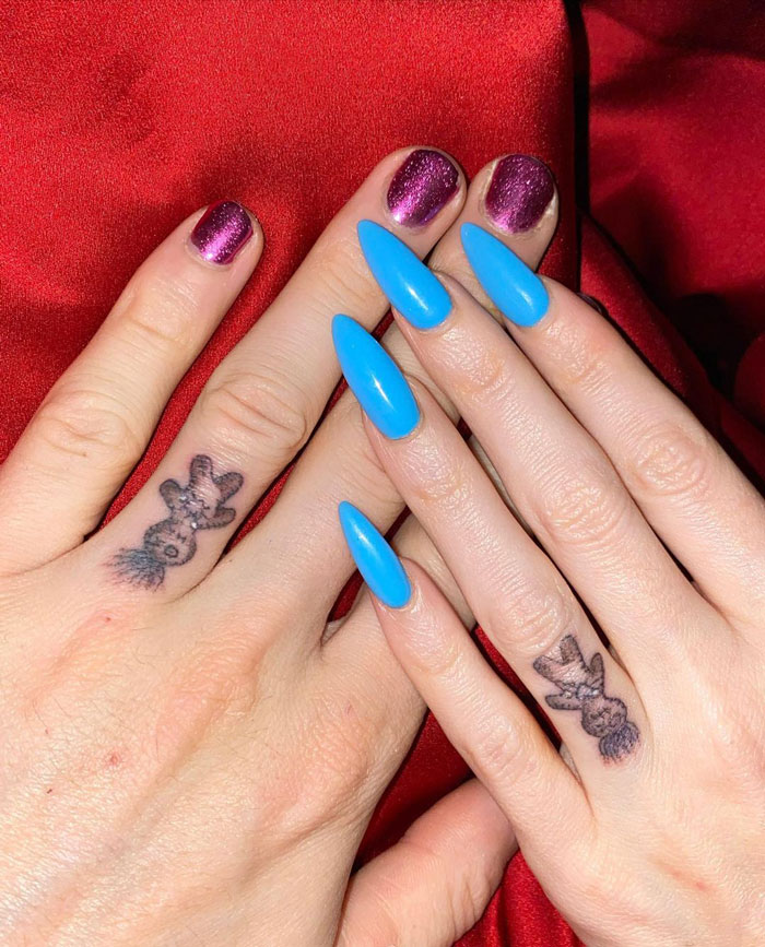 Celebrity tattoos on fingers with vibrant nail colors against a red background.