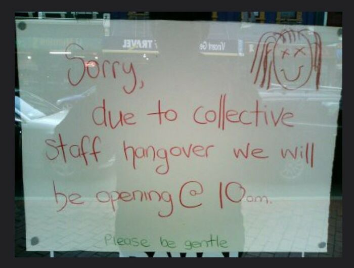 Handwritten sign on window humorously explains delayed opening due to collective staff hangover, a hilariously absurd sign sighting.