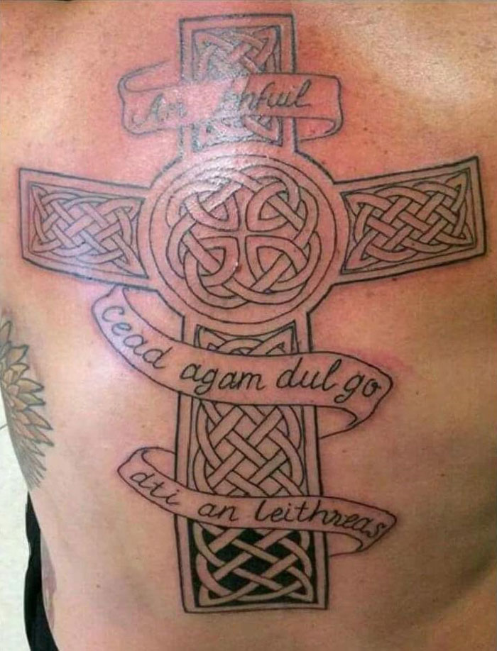 Celtic cross tattoo with humorous phrases, showcasing intricate knotwork on the back.