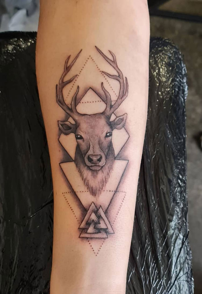 Geometric tattoo of a deer head with triangle patterns on forearm.