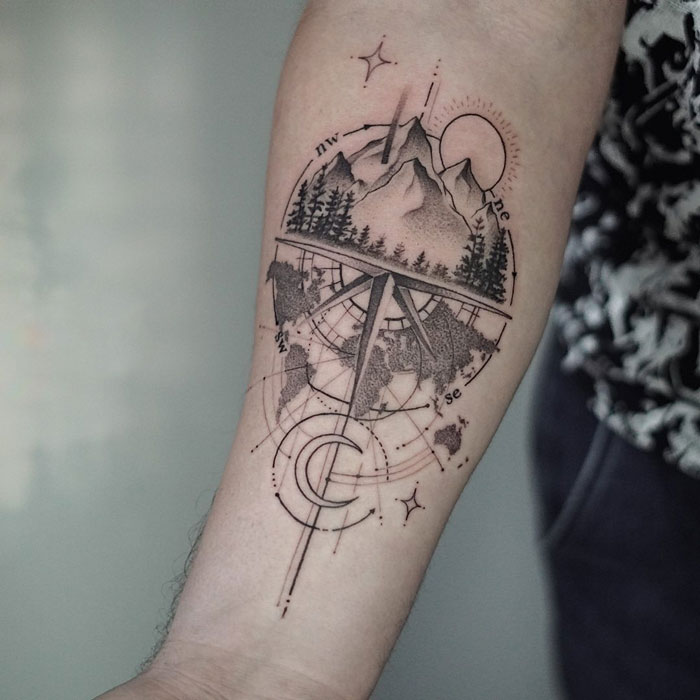 Geometric tattoo with mountains, trees, and compass design on forearm, featuring intricate linework and patterns.