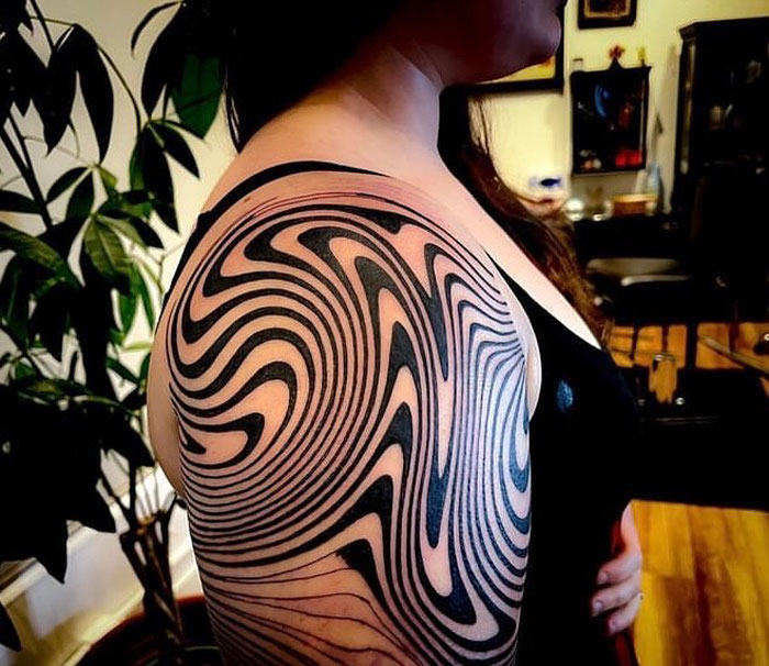 Woman with an intricate geometric tattoo on her arm, featuring bold black swirls.
