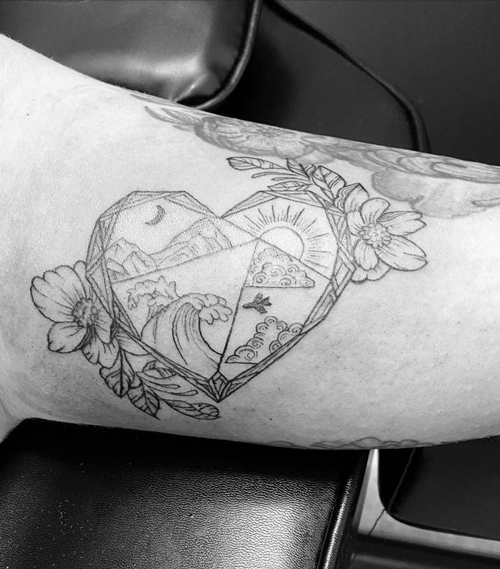Heart-shaped geometric tattoo with nature scenes and flowers on arm, showcasing creativity and artistic design.