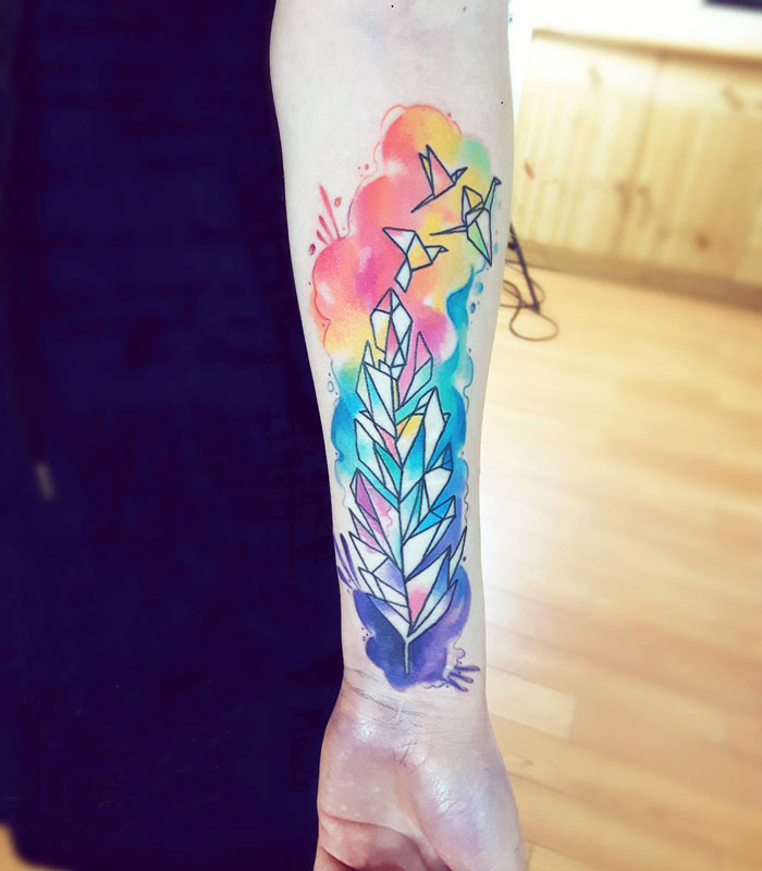 Colorful geometric tattoo featuring a feather and birds on a person's forearm.