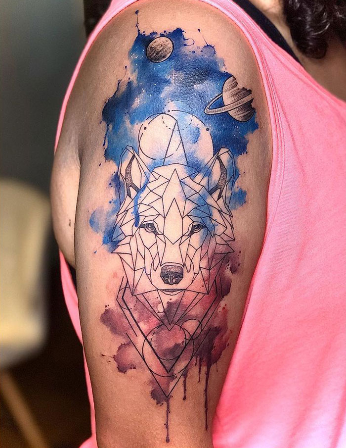 Geometric wolf tattoo on arm with blue and purple galaxy-like background.