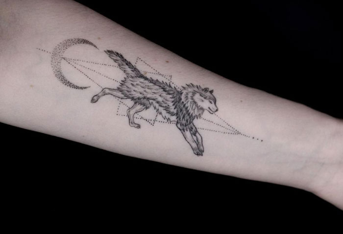 Geometric tattoo of a wolf and crescent moon on forearm, showcasing creativity and intricate shapes.