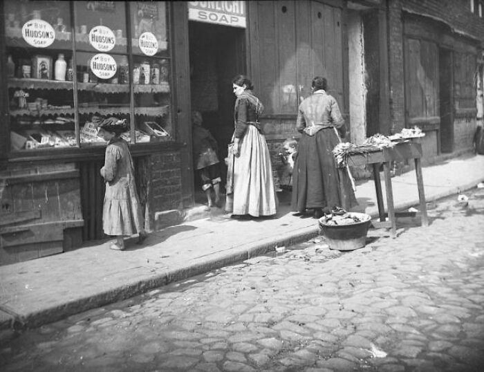 A Young Girl Examines The Window Display Of A City Shop Selling Fresh Vegetables, 1850