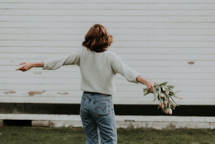 Turned away girl holding a flower bouquet in outstretched arms