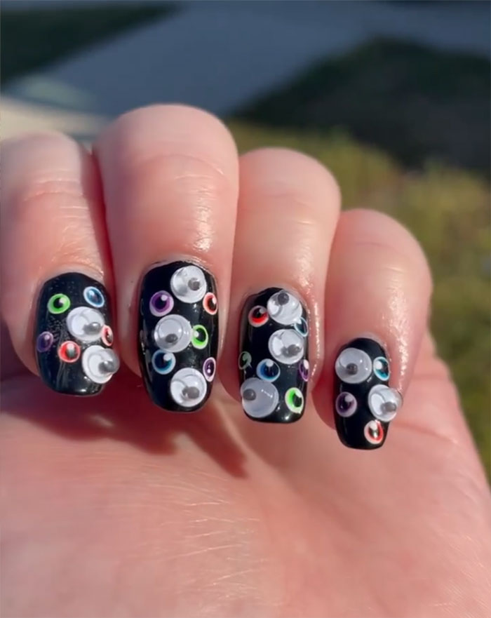 Close-up of nails with black nail art featuring colorful circular designs and 3D embellishments in sunlight.