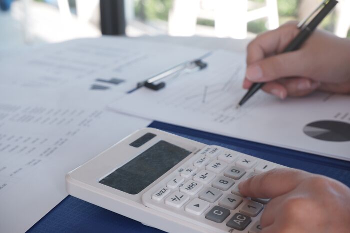 Person using a calculator and pen to review documents, symbolizing people sharing the juiciest pieces of gossip they know.