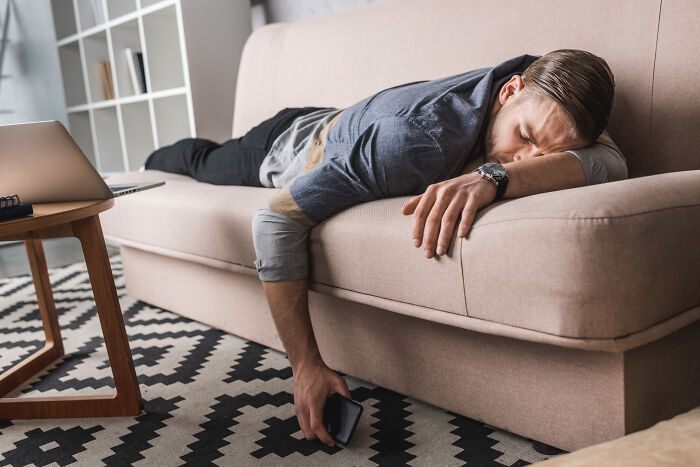Man lying on a couch with a phone in hand, appearing tired, representing people sharing juicy gossip stories.