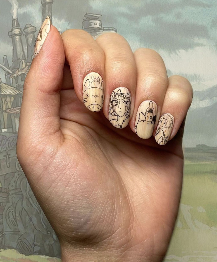 Hand with beige nail art featuring detailed black line anime character designs, showcasing creative nail art ideas.
