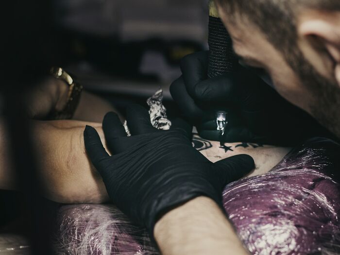 Tattoo artist applying ink design on a person's arm in a studio setting.